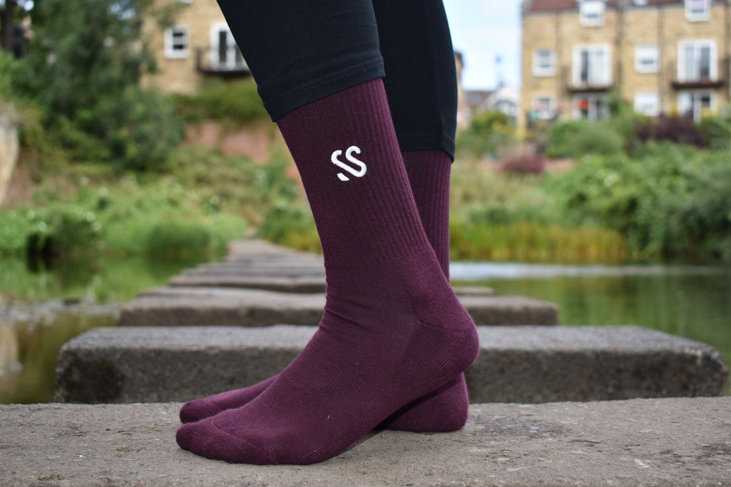 A pair of burgundy combed cotton socks being worn outside by a river
